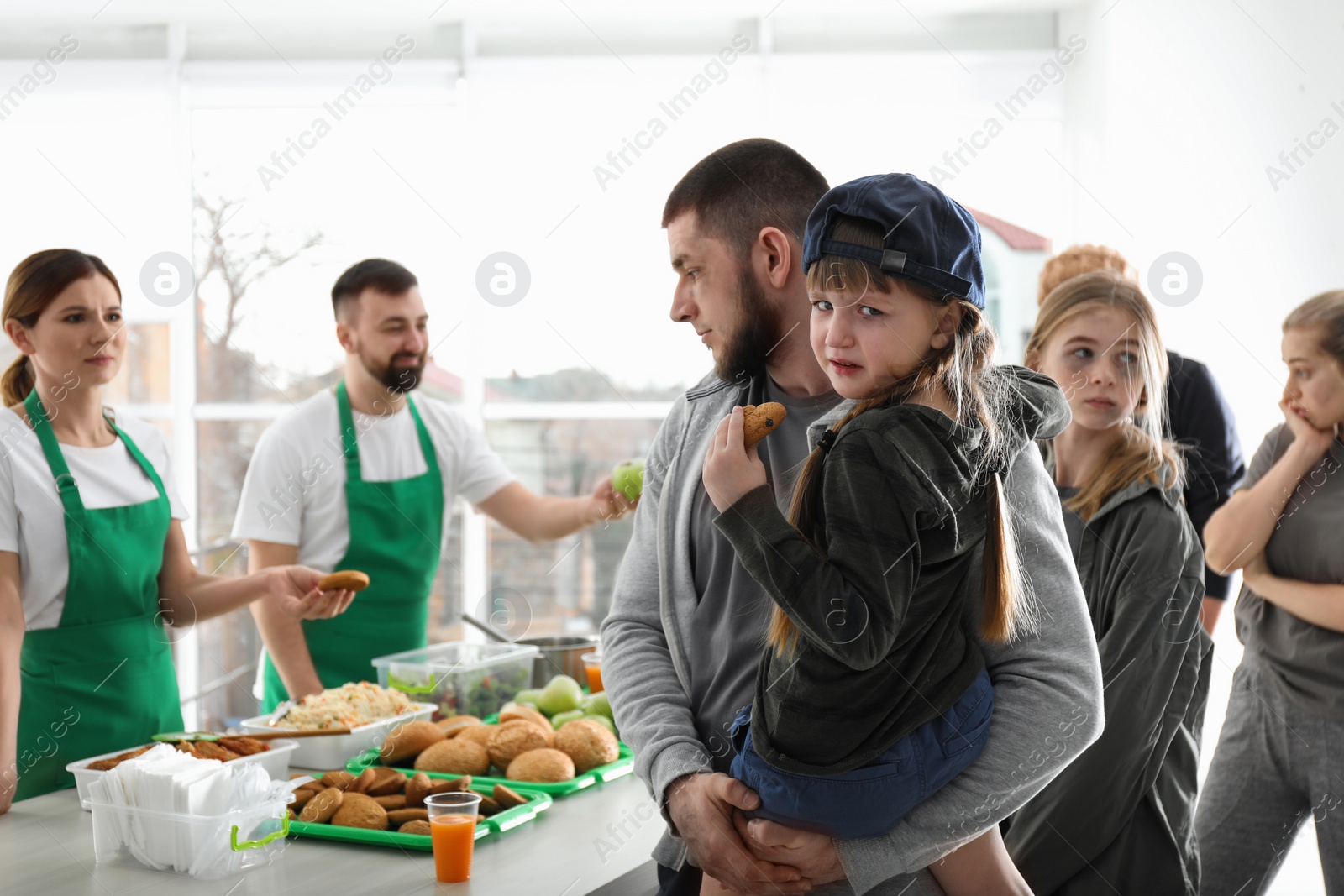 Photo of Father and daughter with other poor people receiving food from volunteers indoors