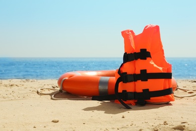 Photo of Orange life jacket and buoy on sandy beach near sea. Emergency rescue equipment