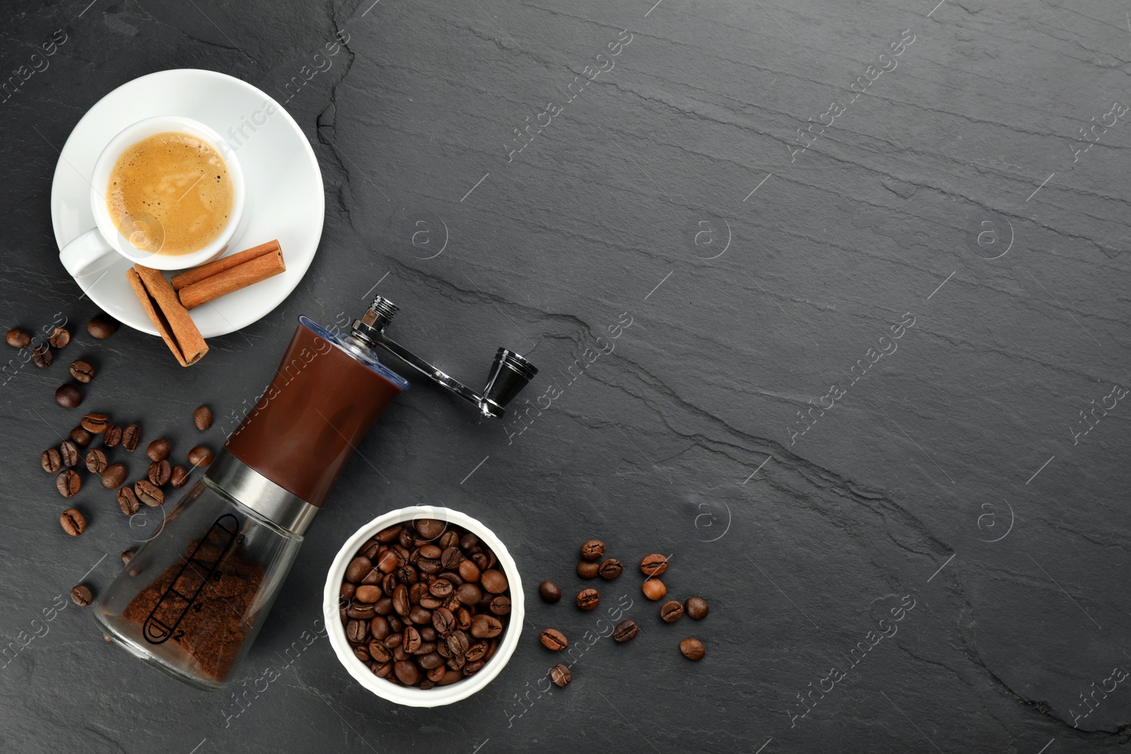 Photo of Modern manual coffee grinder with powder, beans and cup of aromatic drink on black table, flat lay. Space for text