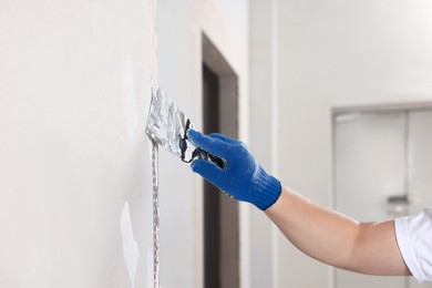 Photo of Man plastering wall with putty knife indoors, closeup. Home renovation