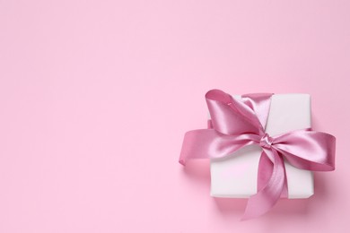 Beautiful gift box with bow on pink background, top view. Space for text