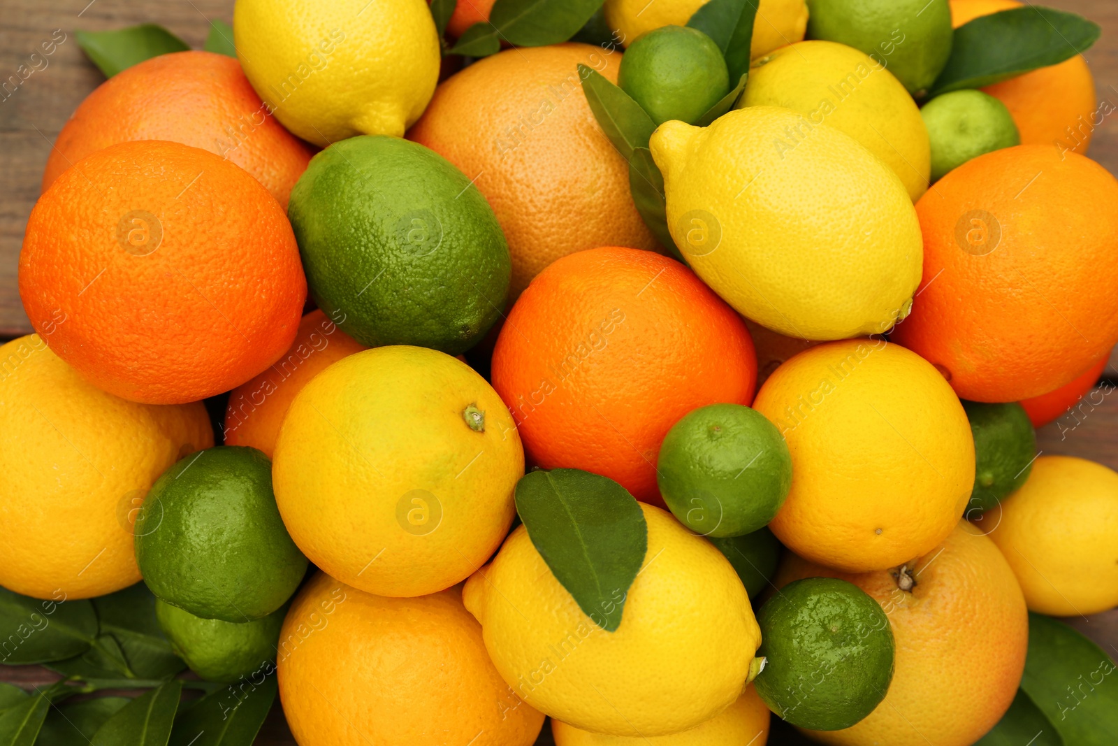 Photo of Different citrus fruits with green leaves on wooden table, top view