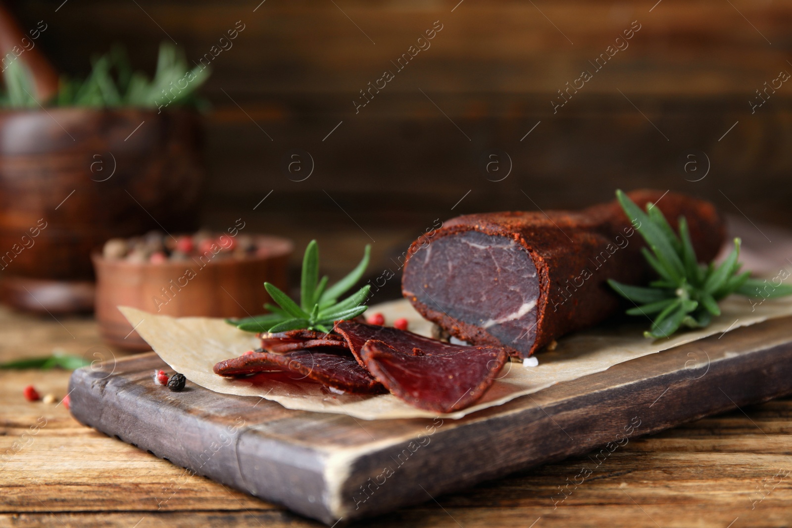 Photo of Delicious dry-cured beef basturma with rosemary and peppercorns on wooden table, closeup