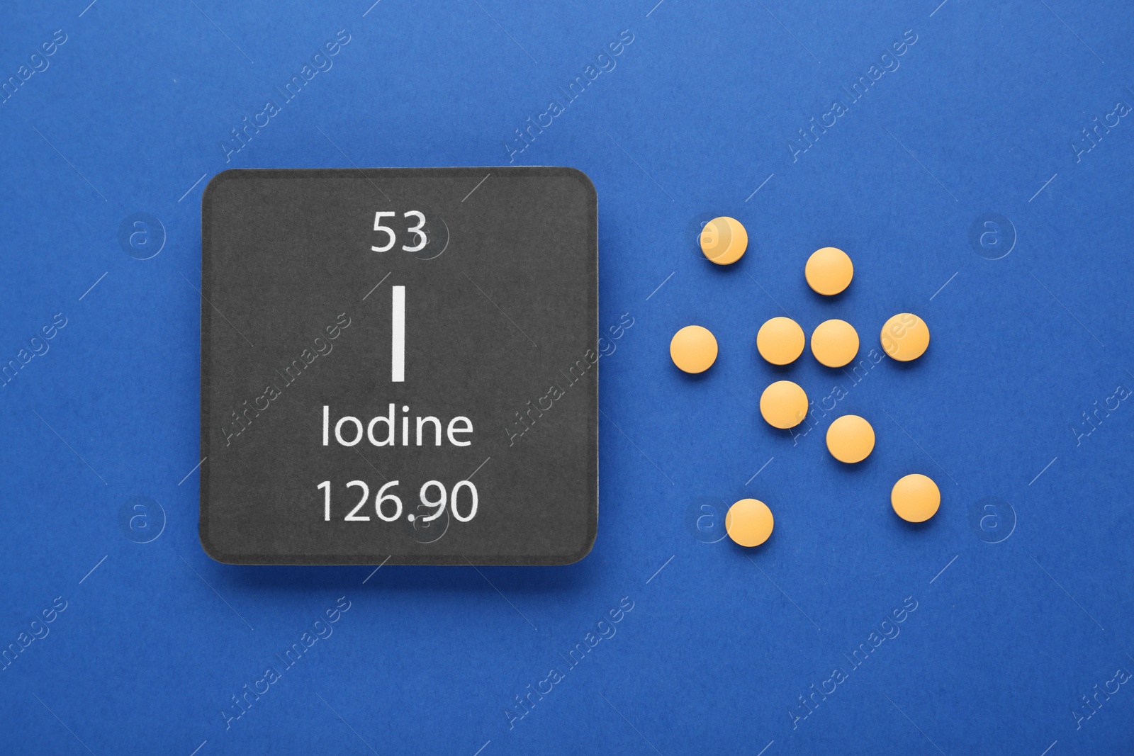 Photo of Card with iodine element and pills on blue background, flat lay