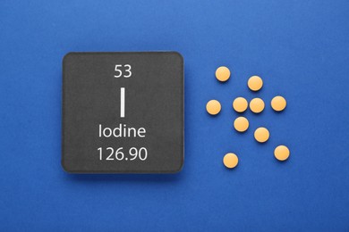 Card with iodine element and pills on blue background, flat lay