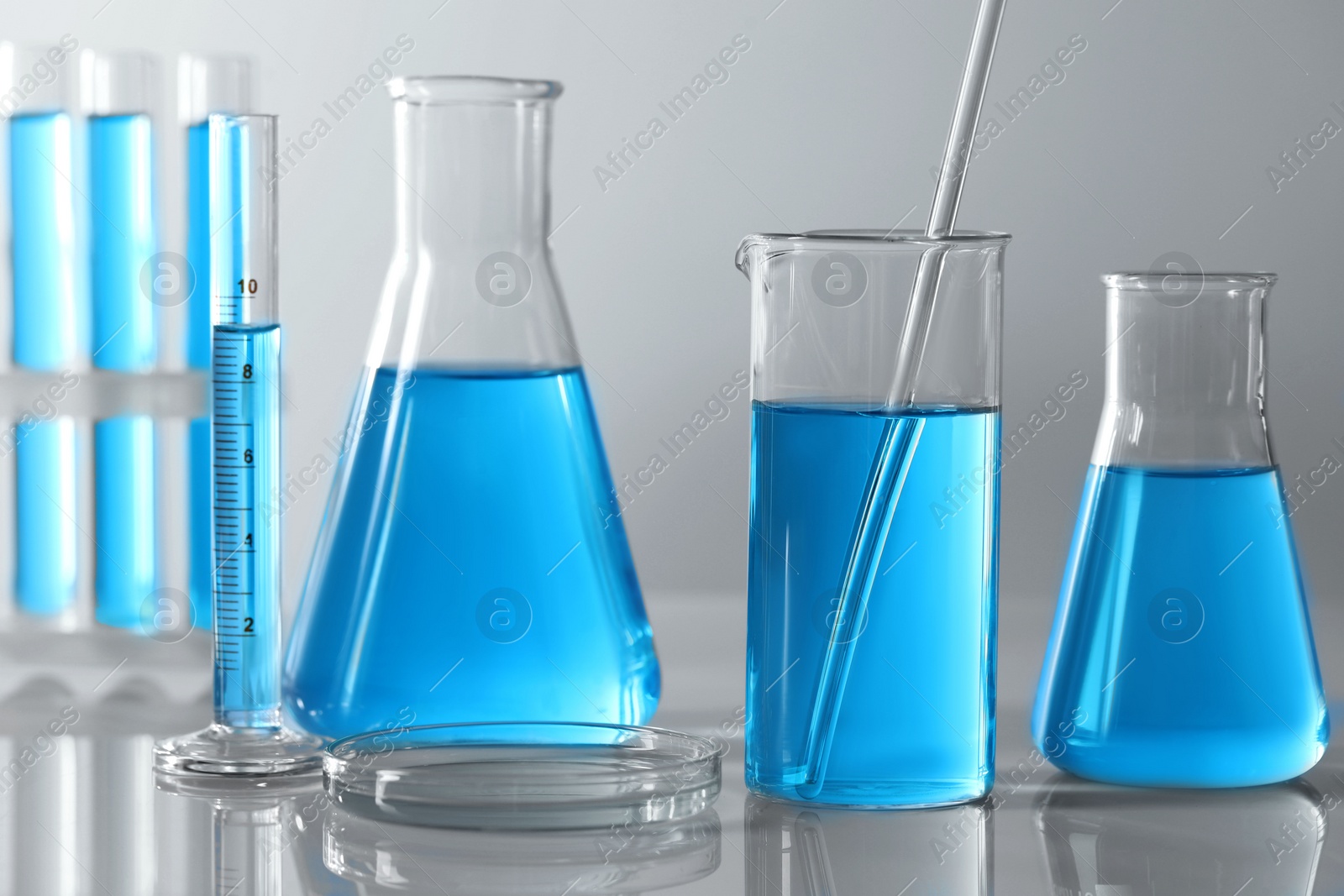 Photo of Different laboratory glassware and test tubes with light blue liquid on table