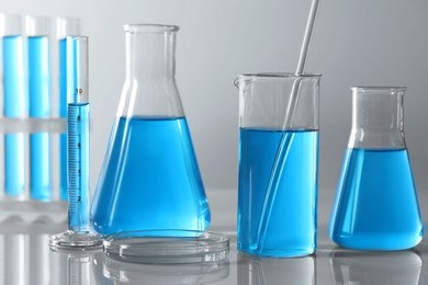Different laboratory glassware and test tubes with light blue liquid on table