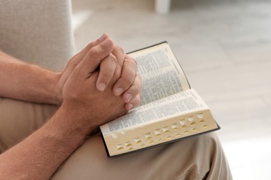 Religious man with Bible praying indoors, closeup