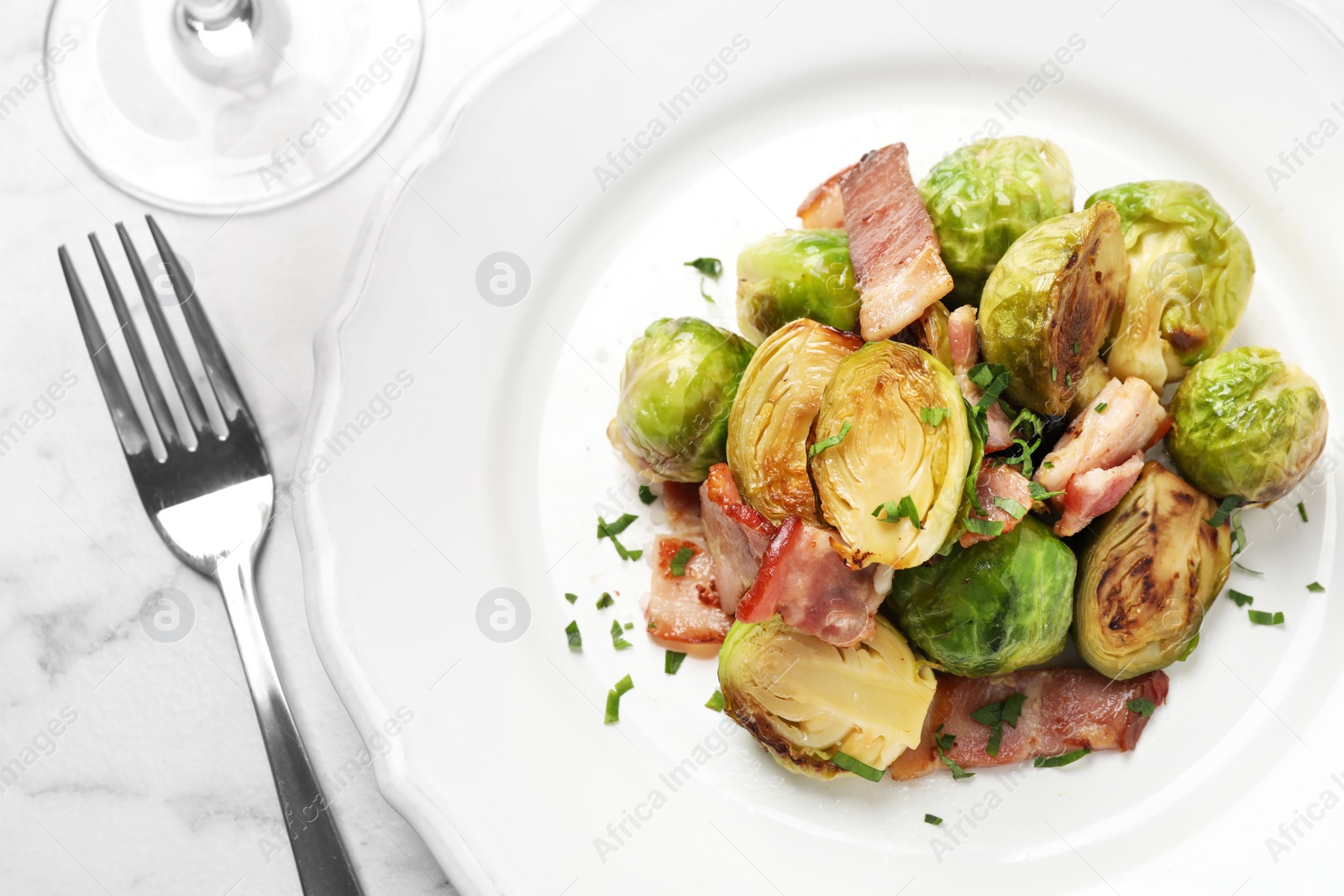 Photo of Delicious Brussels sprouts with bacon served on white table, flat lay