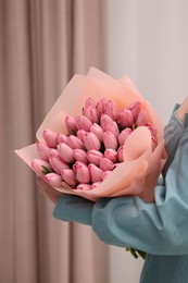 Photo of Woman holding bouquet of pink tulips indoors, closeup