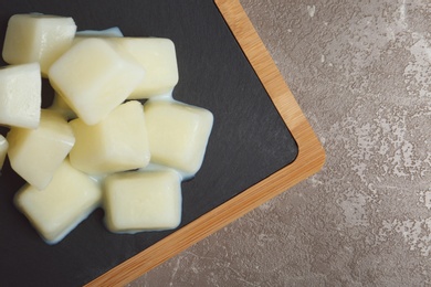 Board with milk ice cubes on grey background, top view. Space for text