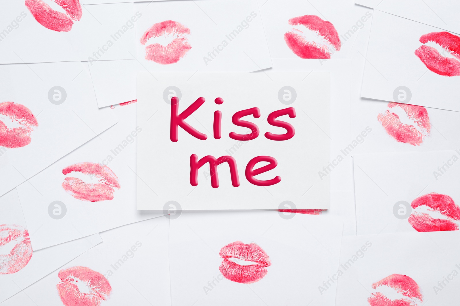 Photo of Card with phrase Kiss Me and lipstick marks on white background, top view