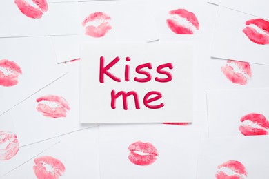 Photo of Card with phrase Kiss Me and lipstick marks on white background, top view