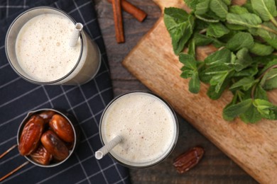 Glasses of delicious date smoothie, dried fruits and mint on wooden table, flat lay