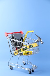 Photo of Small shopping cart with set of construction tools and gloves on light blue background