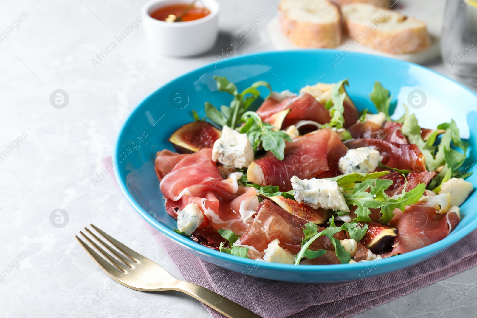 Photo of Salad with ripe figs and prosciutto served on grey marble table, closeup