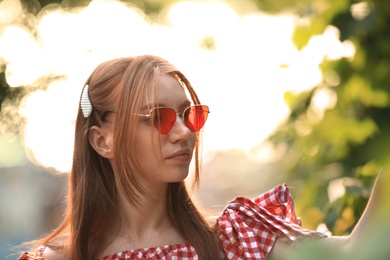 Photo of Beautiful young woman wearing sunglasses on blurred background