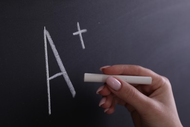 School grade. Teacher writing letter A and plus symbol with chalk on blackboard, closeup