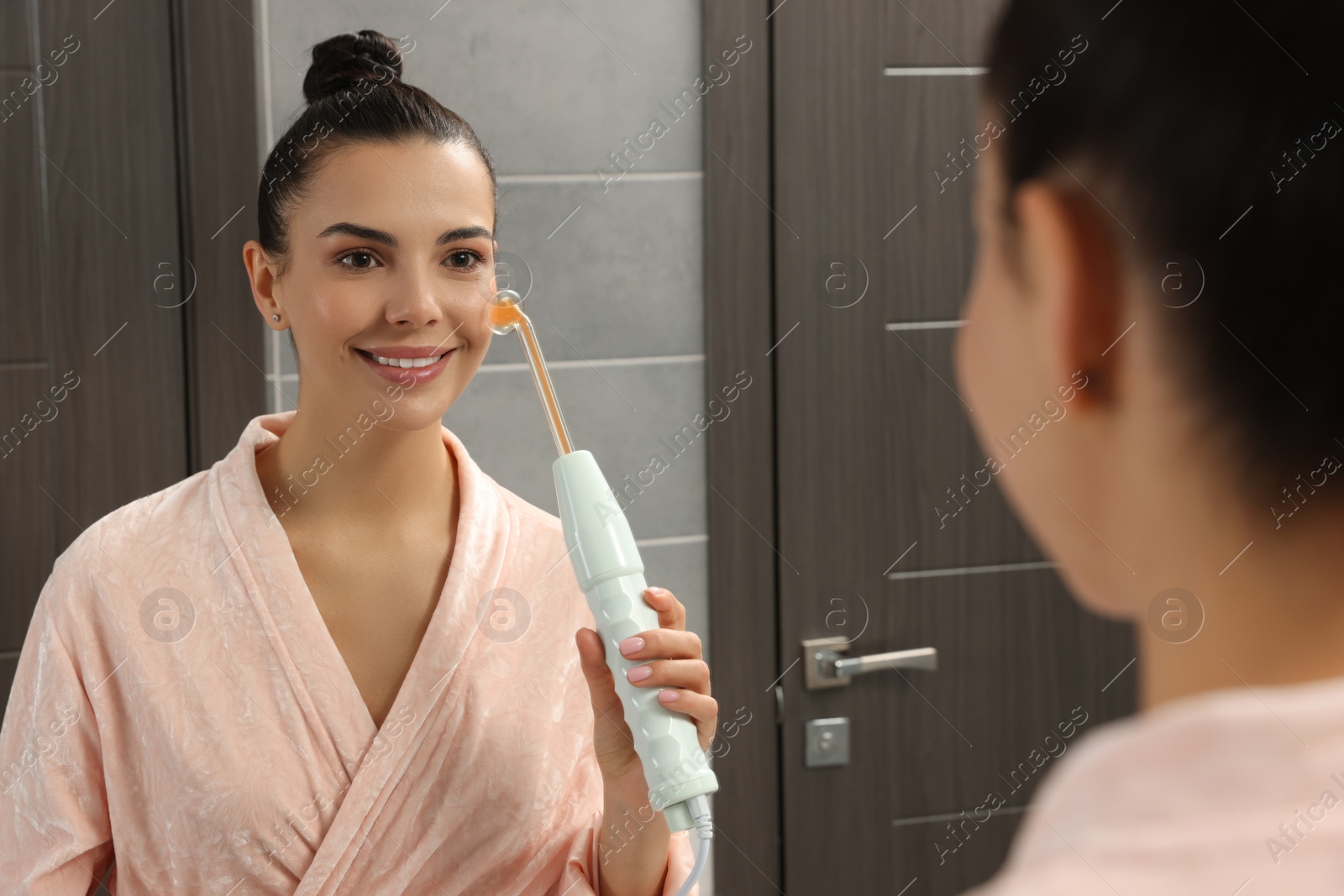 Photo of Woman using high frequency darsonval device near mirror in bathroom