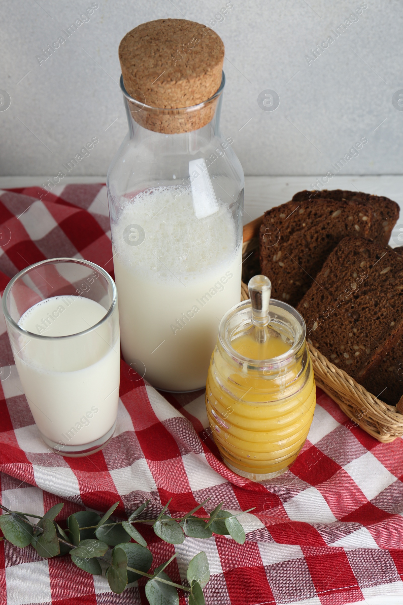 Photo of Jar with tasty honey, milk and bread on checkered cloth