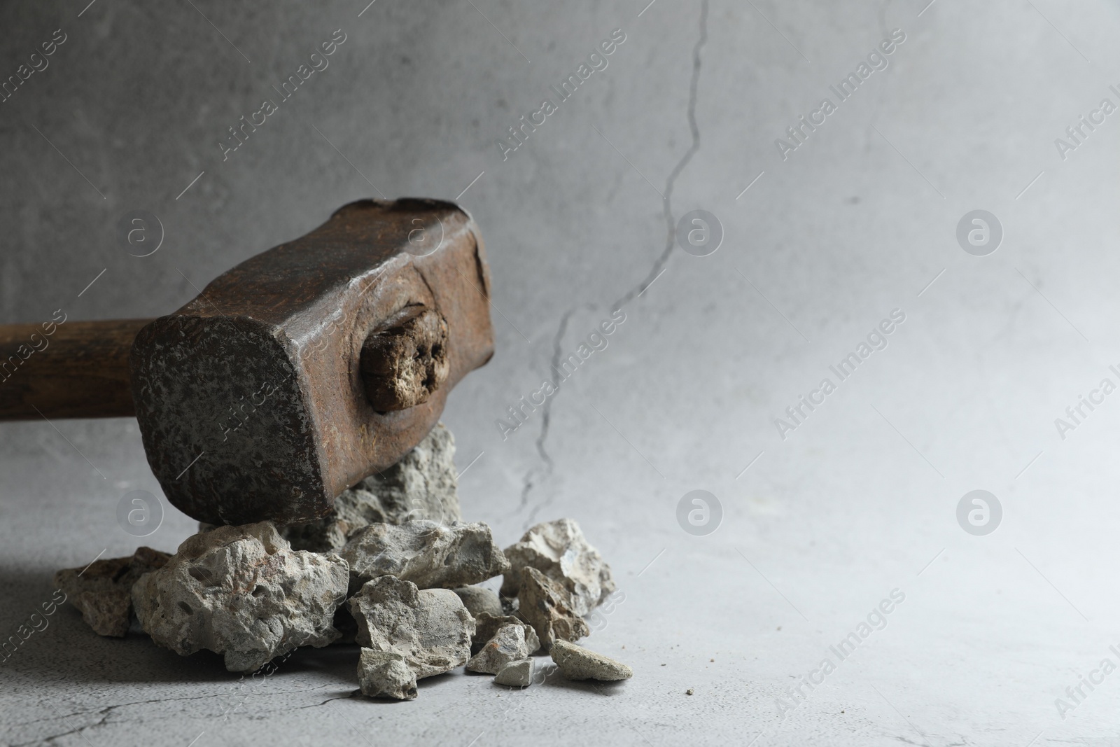 Photo of One sledgehammer and pieces of broken stones on grey background, closeup. Space for text