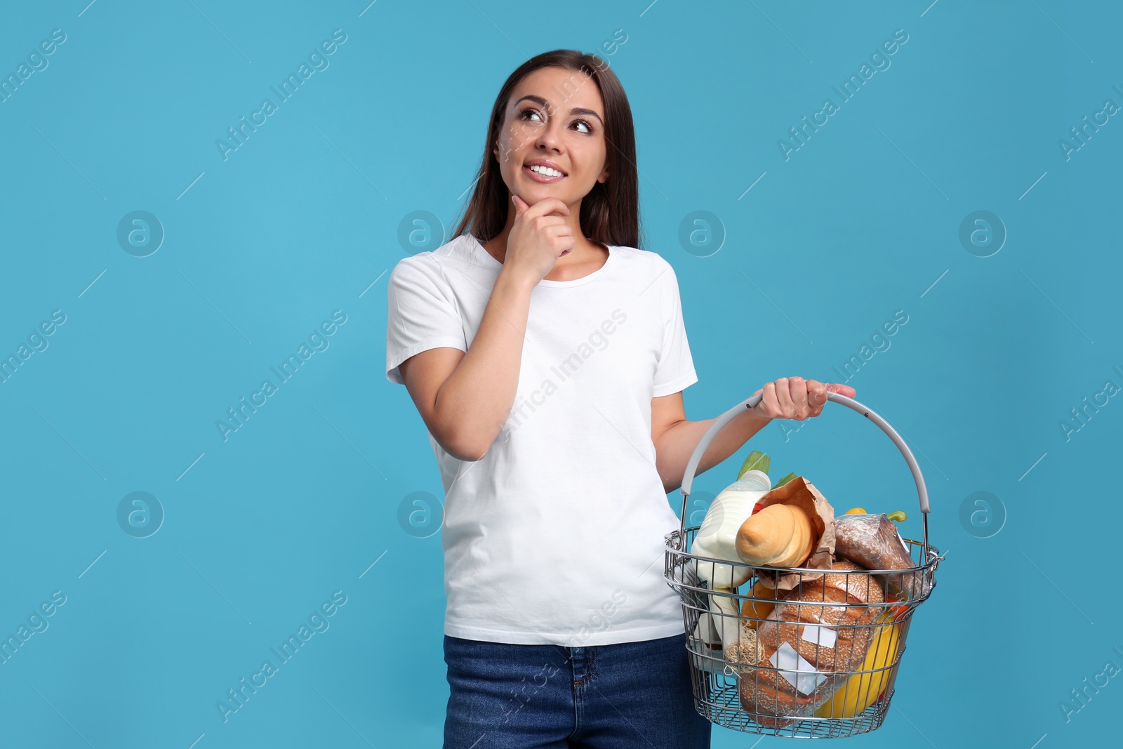 Photo of Young woman with shopping basket full of products on blue background