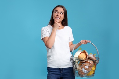 Young woman with shopping basket full of products on blue background