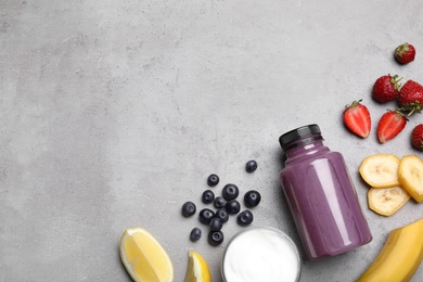 Bottle of acai drink and ingredients on grey background, flat lay. Space for text