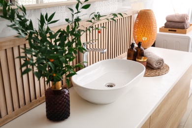 Photo of Vase with beautiful branches and candles near vessel sink in bathroom. Interior design