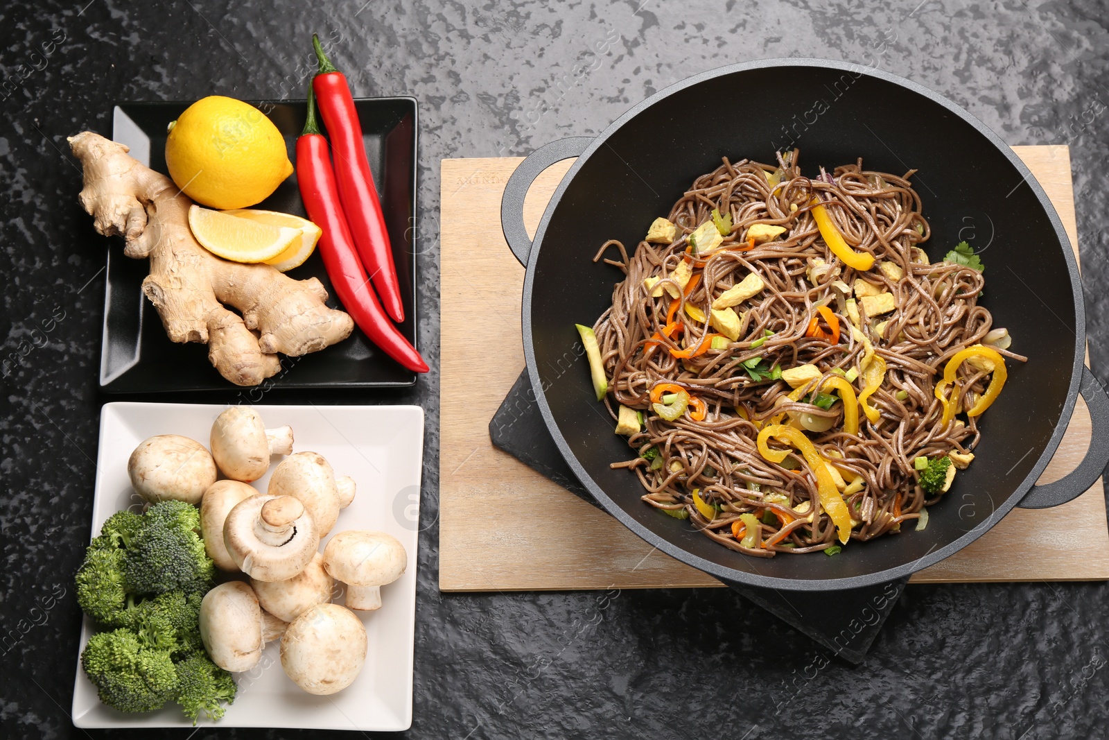 Photo of Stir-fry. Tasty noodles with vegetables, meat in wok and ingredients on dark textured table, flat lay