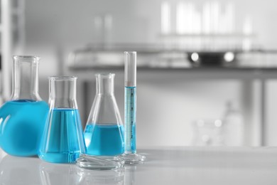 Different glassware with light blue liquid on table in laboratory, space for text