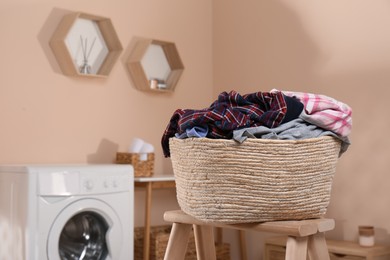 Wicker laundry basket with clothes on wooden stool in bathroom. Space for text