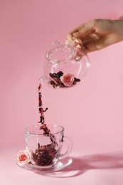 Woman pouring hibiscus tea leaves from teapot into cup on pink background, closeup