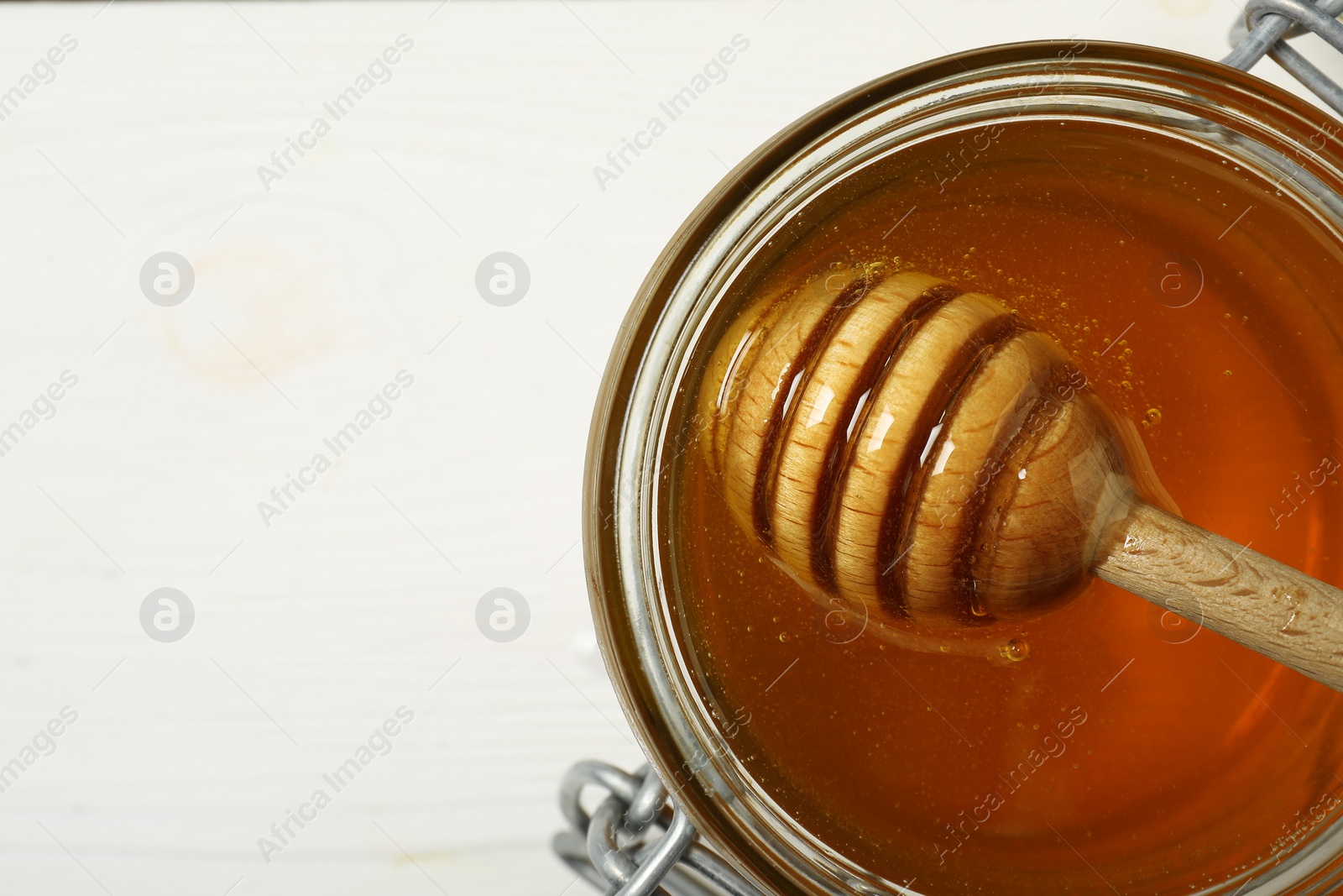 Photo of Dipper with honey in jar on white wooden table, top view. Space for text