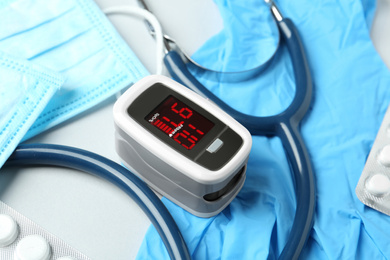 Photo of Modern fingertip pulse oximeter and medical items on white background, closeup