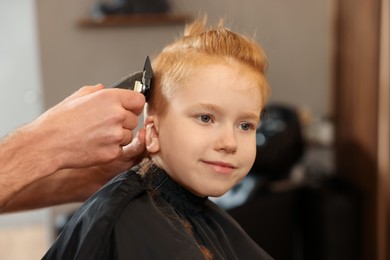 Photo of Professional hairdresser cutting boy's hair in beauty salon, closeup