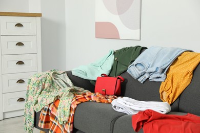 Photo of Messy pile of clothes on sofa in living room