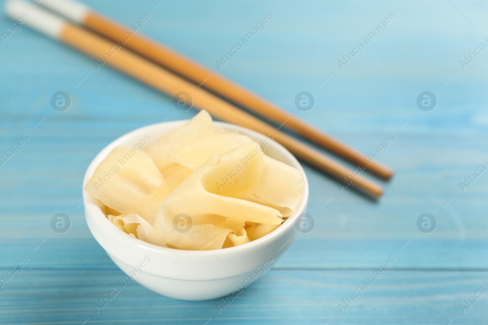 Photo of Spicy pickled ginger and chopsticks on light blue wooden table, space for text