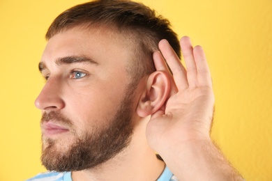 Young man with hearing problem on color background