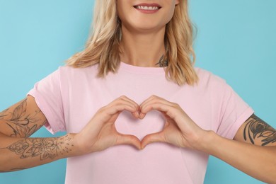 Happy volunteer making heart with her hands on light blue background, closeup