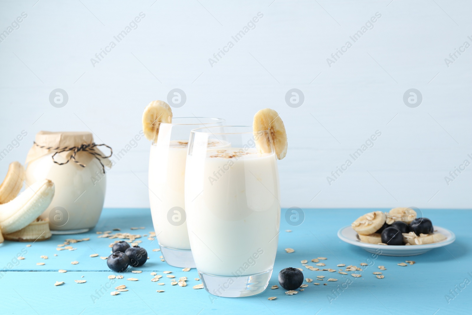 Photo of Tasty yogurt in glasses, oats, banana and blueberries on light blue wooden table