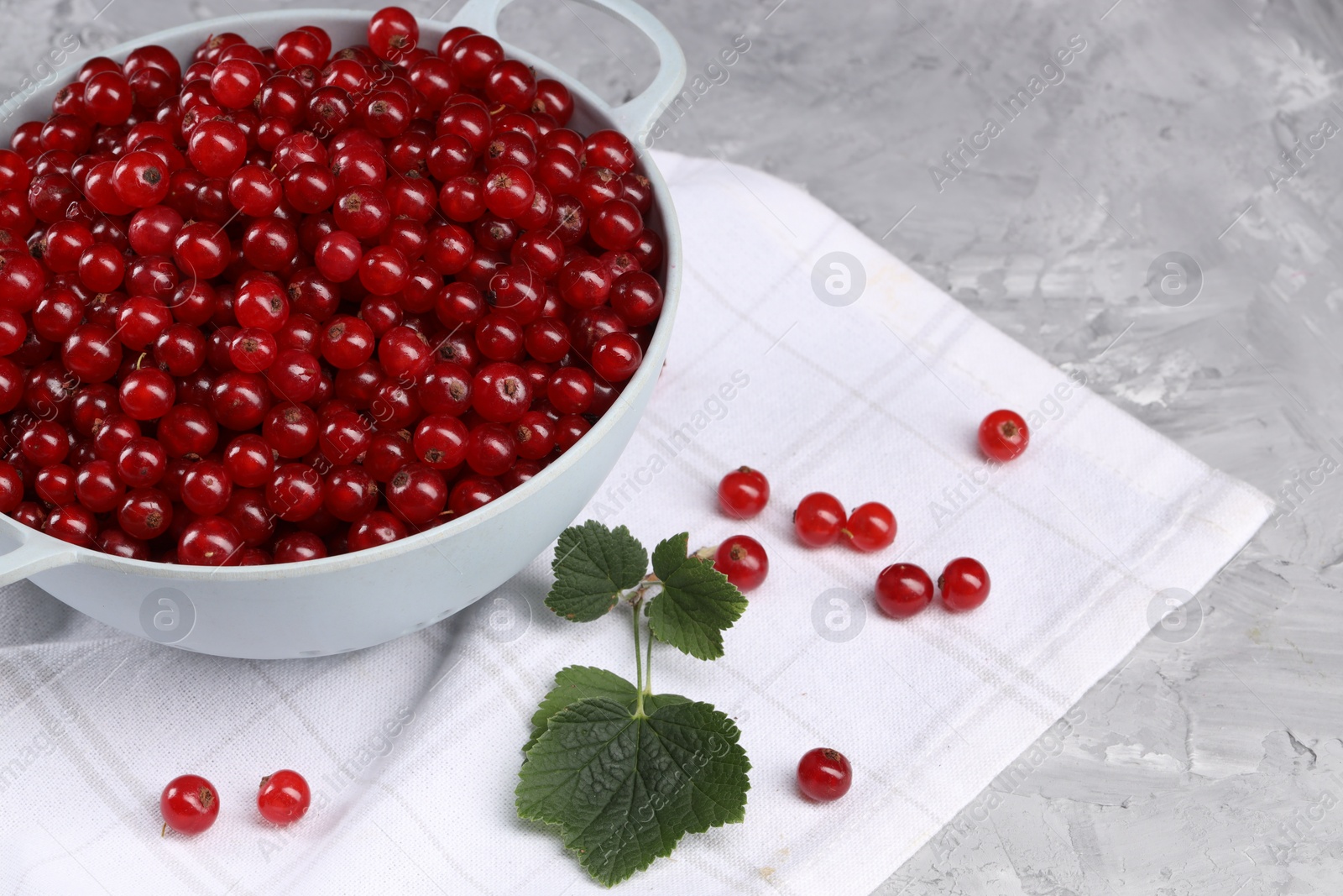 Photo of Ripe red currants in colander and leaves on grey textured table. Space for text