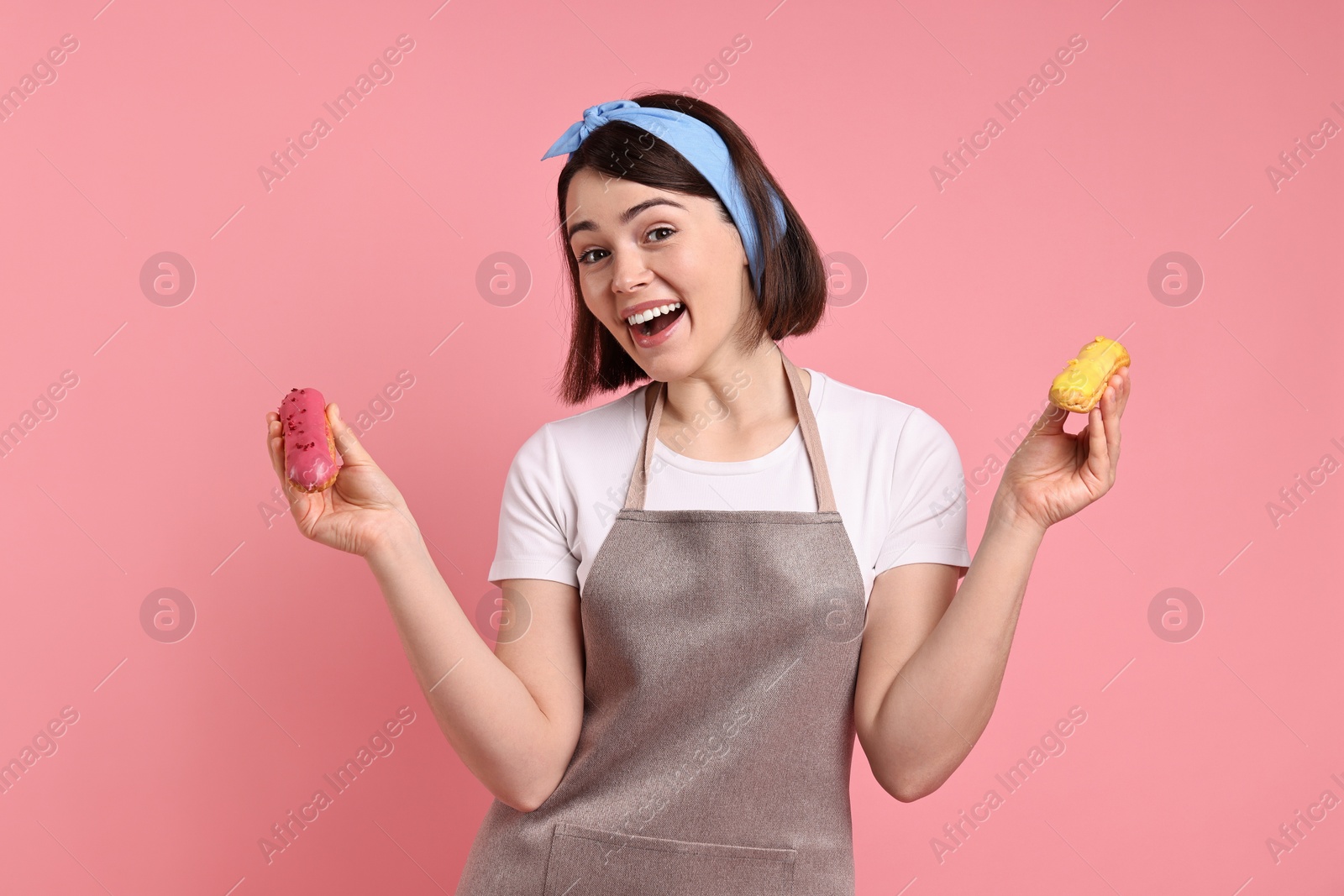 Photo of Happy confectioner with delicious eclairs on pink background