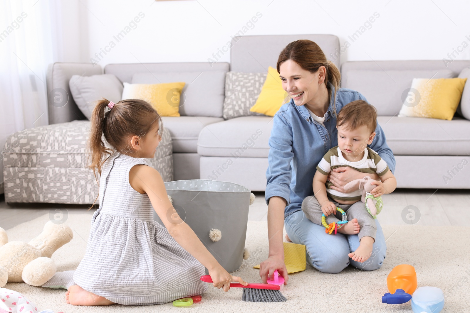 Photo of Housewife with little children cleaning carpet in room