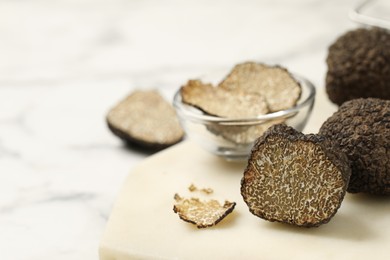 Whole and cut black truffles with board on table, closeup. Space for text