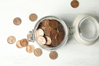 Photo of Glass jar with coins on white wooden table, flat lay
