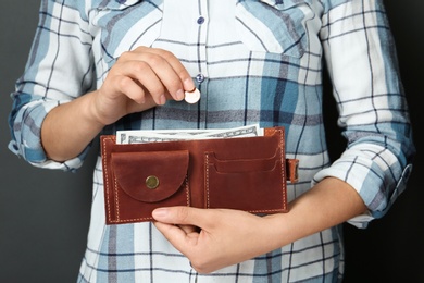 Photo of Young woman putting coin into wallet on grey background, closeup