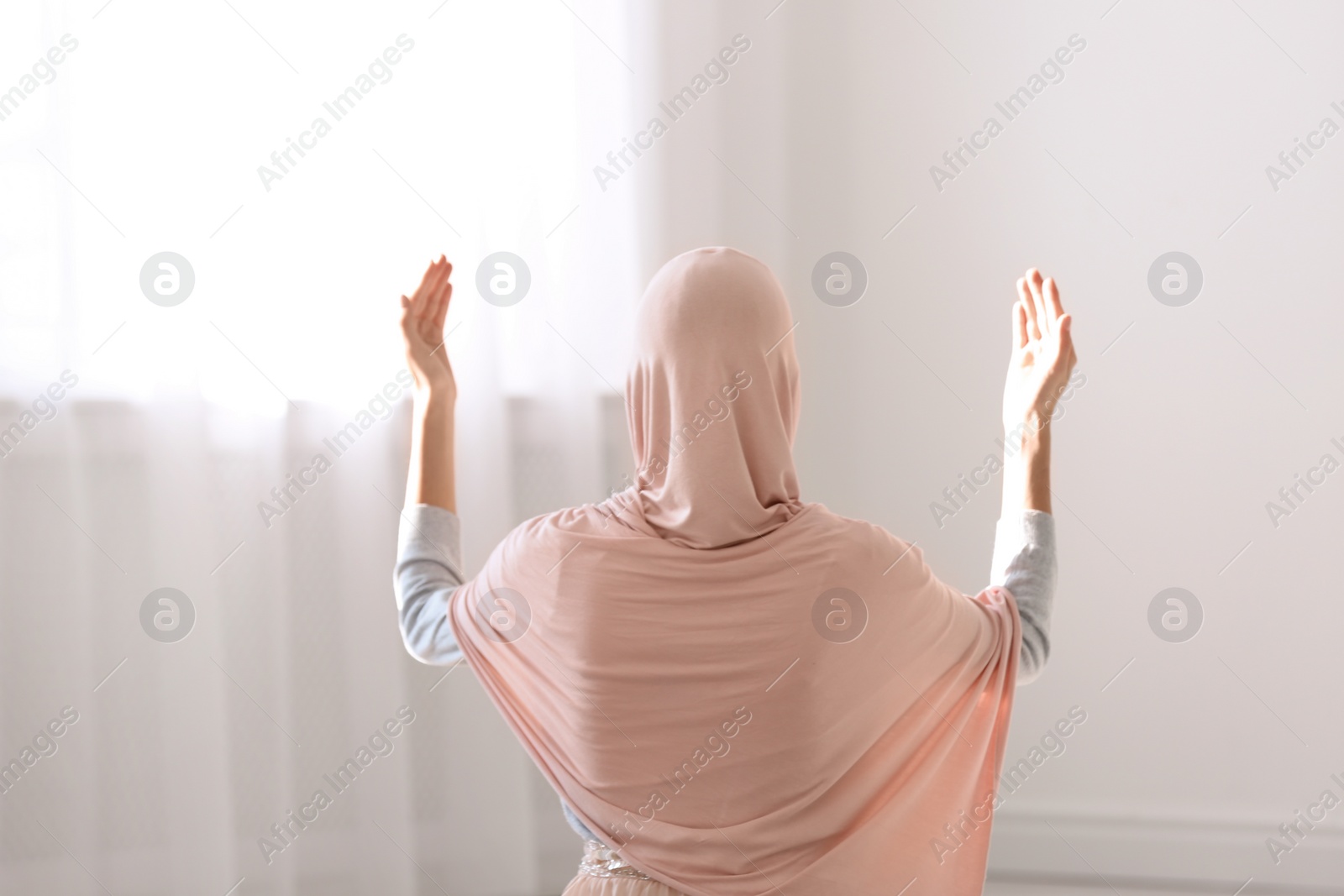 Photo of Young Muslim woman in hijab praying indoors