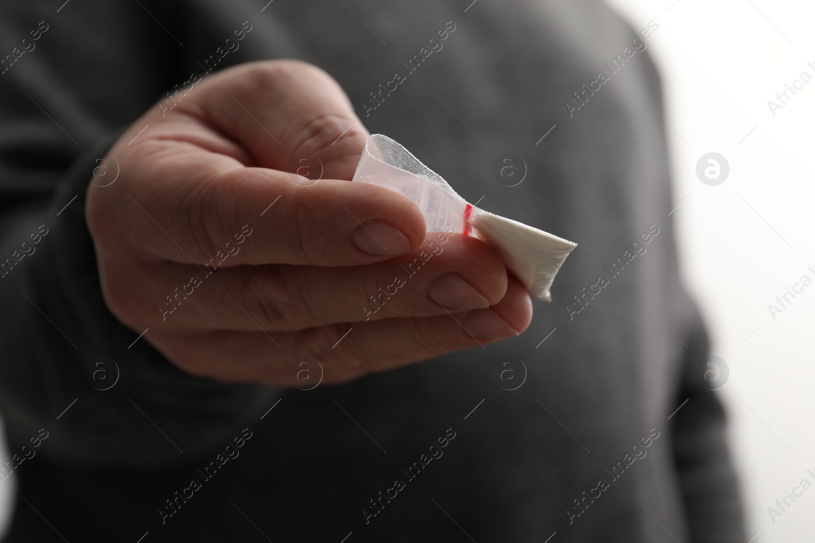 Photo of Drug addiction. Man with plastic bag of cocaine on light background, closeup