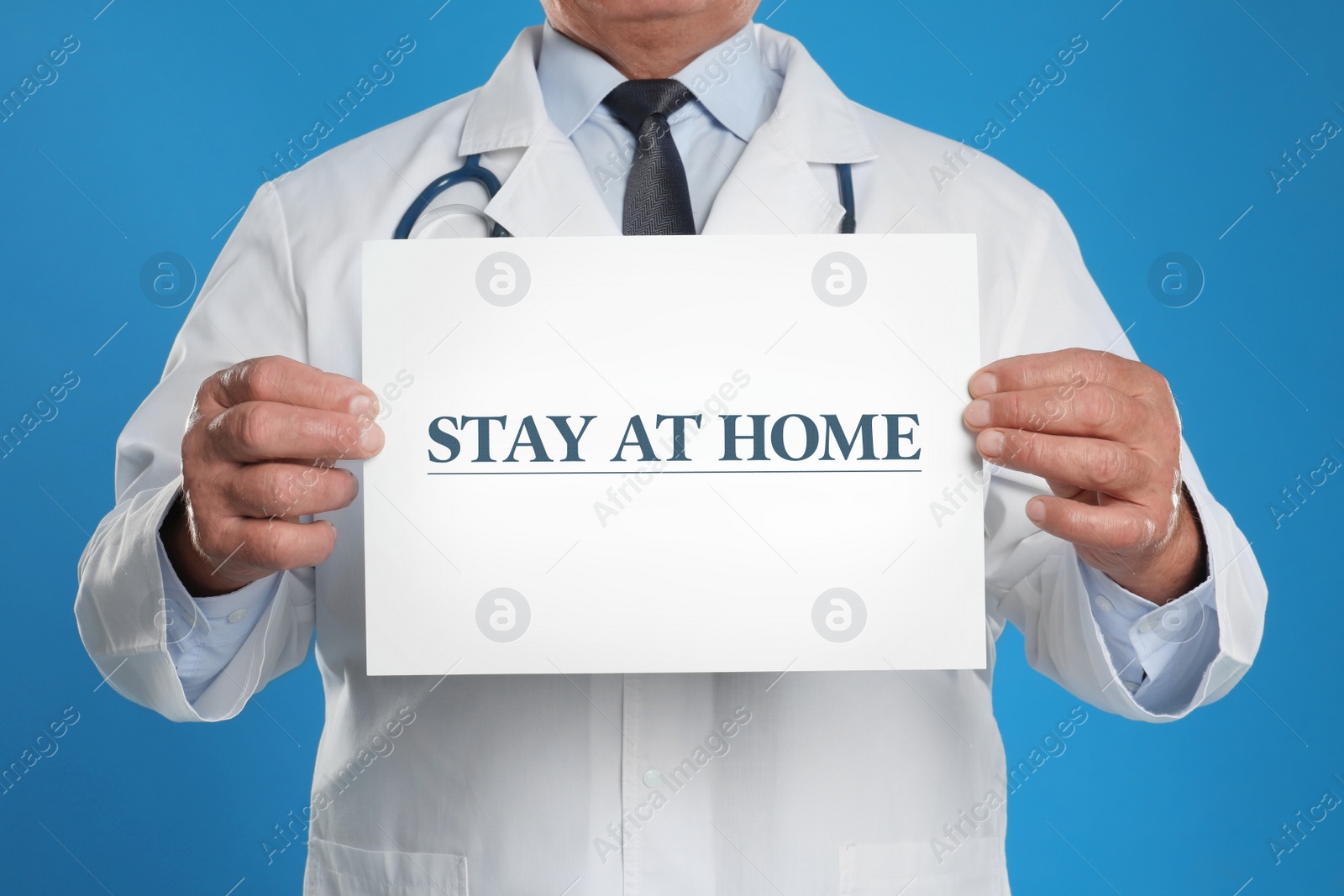 Image of Doctor holding sign with text STAY AT HOME on blue background, closeup. Quarantine during coronavirus outbreak